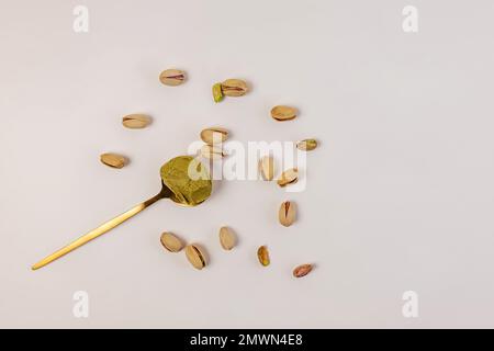 Pâte de pistaches dans la cuillère et pistaches dispersées sur fond blanc Banque D'Images