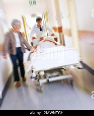 Urgence. un malade sur un lit roulant à grande vitesse à travers un couloir d'hôpital avec sa femme à ses côtés. Banque D'Images