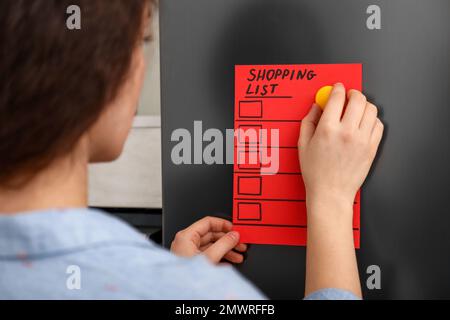 Femme mettant la liste d'achats sur la porte du réfrigérateur, à proximité Banque D'Images