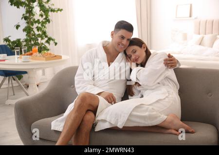 Couple heureux dans des peignoirs sur le canapé à la maison Banque D'Images