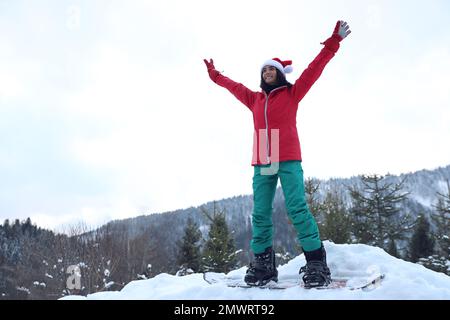 Un jeune snowboardeur porte un chapeau de père Noël sur une colline enneigée. Vacances d'hiver Banque D'Images