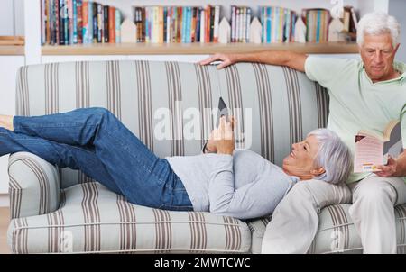 Maintenant, nous pouvons lire le même livre ensemble. Un homme âgé lisant un livre tandis que sa femme lit d'un ereader. Banque D'Images