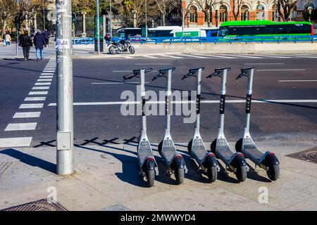 Vue de quatre scooters électriques garés au feu de circulation avec des personnes traversant la route. Banque D'Images