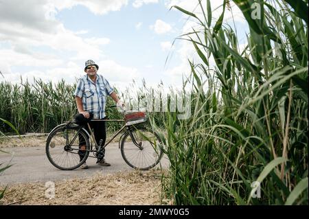 Zaporizhzhia, Ukraine, 1 juillet 2022 : un homme tient une bicyclette, roseaux au premier plan et en arrière-plan. Banque D'Images