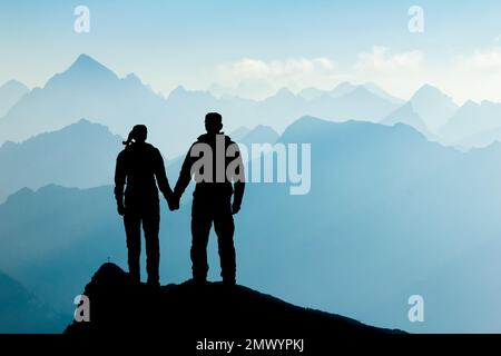 Silhouette couple d'homme et de femme atteignant le sommet de la montagne jouissant de la liberté et regardant vers les silhouettes de montagne bleues et le lever du soleil. Alpes, Allgaeu Banque D'Images