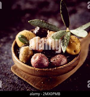 Bouquet de délicieux types d'olives marinées avec assaisonnement et feuilles vertes servi sur une spatule en bois dans une cuisine légère Banque D'Images