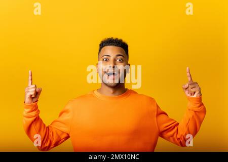 Un Indien attrayant avec une expression faciale stupéfiant pointant vers le haut avec les deux doigts, présentant l'espace de copie. Studio d'intérieur isolé sur fond jaune Banque D'Images