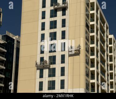 Dubaï, Émirats arabes Unis - 7th janvier 2022 : ouvriers de la construction peignant la façade extérieure d'un immeuble résidentiel, abaissé sur suspension sca Banque D'Images