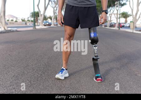 Croissez un sportif anonyme dans des vêtements de sport avec une jambe artificielle debout sur la route asphaltée pendant l'entraînement de course dans la rue de ville Banque D'Images