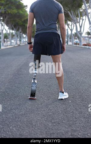 Vue arrière d'un athlète masculin anonyme en vêtements de sport avec jambe en lame artificielle debout dans la rue et se préparant à courir en ville Banque D'Images