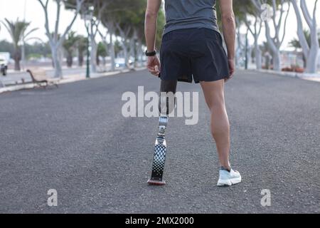 Vue arrière de Crop anonyme masculin amputé de vêtements de sport debout sur la route se préparant à courir dans le parc de la ville Banque D'Images