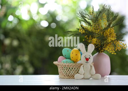 Jouet lapin de Pâques, œufs teints et fleurs sur une table en bois blanc sur fond vert flou. Espace pour le texte Banque D'Images