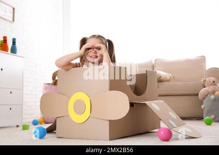 Mignon petit enfant jouant avec un avion en carton à la maison Banque D'Images