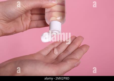 Femme appliquant du gel antiseptique sur fond rose, gros plan Banque D'Images