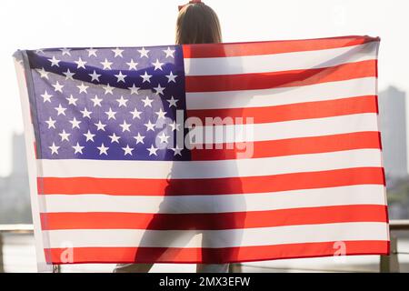 Vacances patriotiques. Bonne jeune femme caucasienne élégante avec drapeau américain à l'extérieur au coucher du soleil. Les Etats-Unis célèbrent l'indépendance le 4th juillet. Banque D'Images