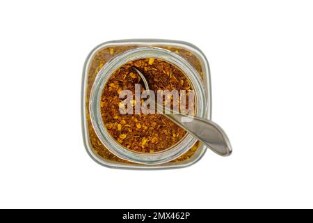 Poudre de Chili dans un pot en verre avec une cuillère, vue de dessus, isolé sur fond blanc Banque D'Images
