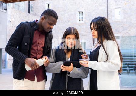 Collègues utilisant une tablette en dehors du bureau. Groupe d'amis et de partenaires discutant au travail en plein air dans la ville. Diversité ethnique et inclusion sociale. Banque D'Images