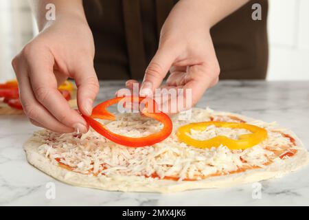 Femme ajoutant du poivron à la table en marbre blanc de pizza, gros plan Banque D'Images