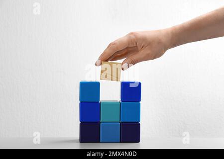 Femme mettant bloc de bois aux cubes colorés sur fond blanc, gros plan. Concept de promotion de carrière Banque D'Images