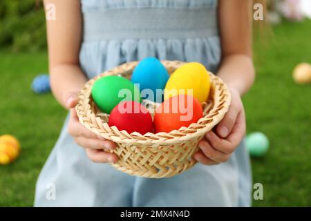 Petite fille mignonne avec panier plein d'oeufs de Pâques à l'extérieur, gros plan Banque D'Images