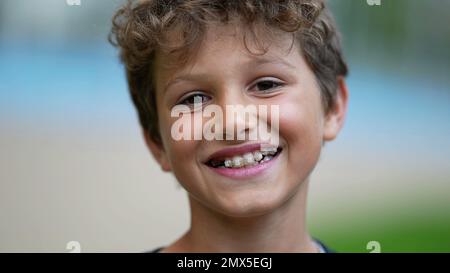 Portrait de jeune garçon heureux visage gros plan souriant dehors. Un beau préadolescent de sexe masculin portant des bretelles regardant l'appareil photo Banque D'Images