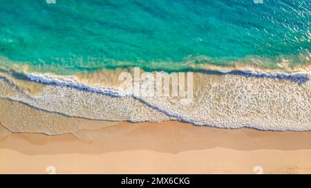 Gros plan sur les vagues de l'océan qui s'enroulent sur une belle plage de sable rose au lever du soleil. Côte sablonneuse avec vagues de mer turquiose blanches. Vague douce de la mer sur une plage de sable avec de la mousse blanche et propre Banque D'Images