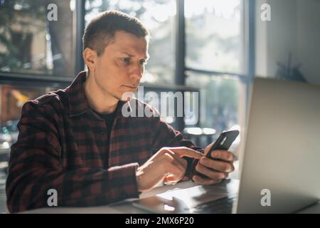Homme utilisant un smartphone moderne et regarde l'écran assis dans un café. Banque D'Images