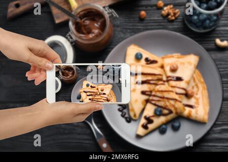 Blogueur de nourriture prenant la photo de délicieux crêpes fines à la table en bois, gros plan Banque D'Images