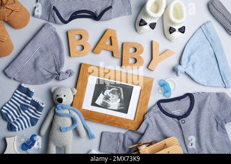 Composition Flat Lay avec vêtements pour enfants, échographie photo et mot bébé sur fond clair Banque D'Images