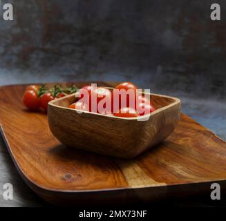 Tomates Aromatico sur un plateau en bois, certaines sur la vigne autres dans un bol en bois. Banque D'Images