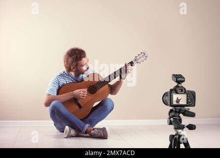 Professeur de musique enregistrant la leçon de guitare près du mur beige Banque D'Images