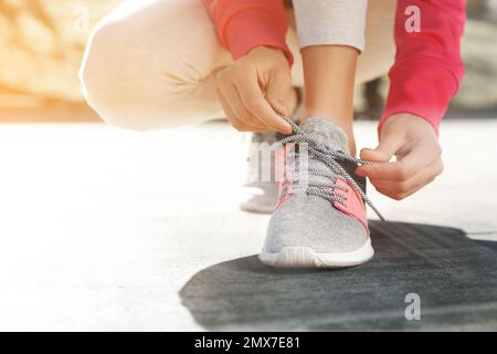 Femme sportive nouant des lacets à l'extérieur le jour ensoleillé, gros plan Banque D'Images