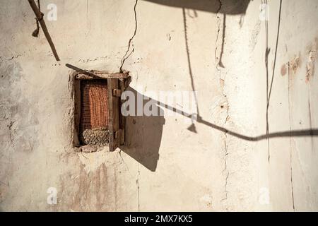 Mur blanc blanchi à la chaux et vieilli avec une petite fenêtre en bois et un volet avec jeu d'ombres sur le mur Banque D'Images