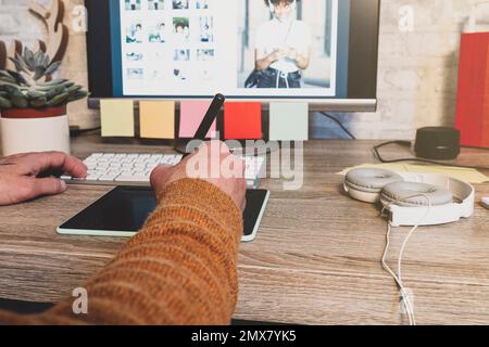 Jeune photographe hippster utilisant une tablette graphique numérique tout en travaillant dans un bureau moderne, retouche professionnelle assis dans un espace de travail moderne avec du bois Banque D'Images