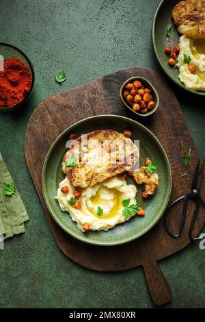 Vue de dessus de délicieux chou-fleur rôti avec purée de pommes de terre et harissa épicée pois chiches servis sur une planche à découper en bois sur table Banque D'Images