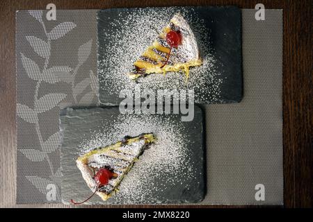 Deux morceaux de cheesecake avec cerises sur des planches de service en pierre noire sur la table dans le café. Vue de dessus. Gros plan. Mise au point sélective. Banque D'Images