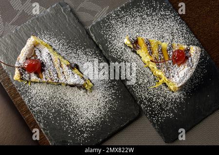 Deux morceaux de cheesecake avec cerises sur des planches de service en pierre noire sur la table dans le café. Vue de dessus. Gros plan. Mise au point sélective. Banque D'Images