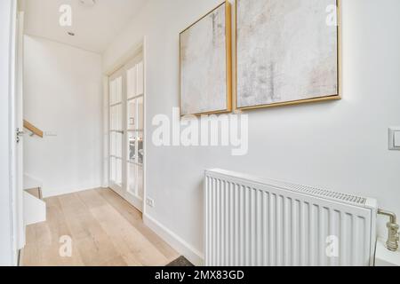 Design intérieur du couloir avec radiateur placé sous les photos sur le mur blanc près de la porte contre les escaliers dans la maison lumineuse Banque D'Images