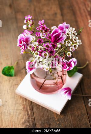 Vue d'en haut du magnifique bouquet de fleurs roses, de cires blanches et de fleurs de cyclamen violets dans un vase en verre. Concept d'arrangement floristique du printemps. Banque D'Images