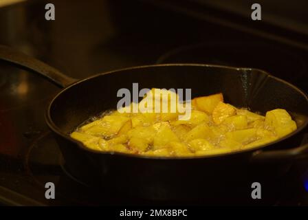 Faire frire des pommes de terre jaunes avec de la graisse de canard dans une poêle en fonte noire sur un poêle en vitrocéramique. Banque D'Images