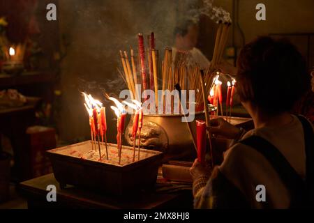 Une femme allume un encens brûlant pour la prière dans un temple bouddhiste de Hong Kong. Banque D'Images