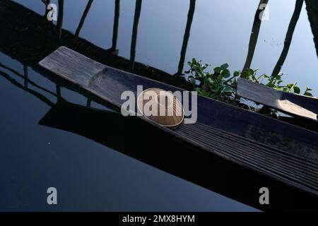 Un chapeau conique solitaire en bambou se trouve à l'extrémité d'un canoë traditionnel en bois dans un village flottant sur le lac Inle, Myanmar (Birmanie). Banque D'Images