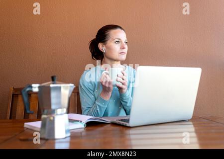 Femme assise dans son pyjama travaillant sur son ordinateur portable et buvant une tasse de café. Banque D'Images