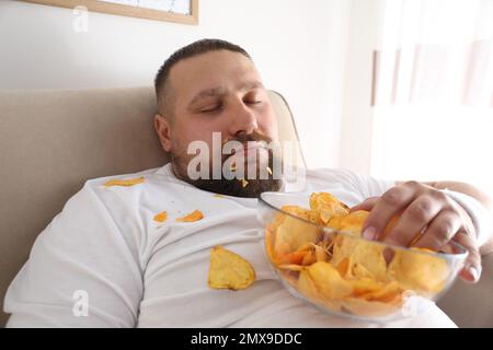 Paresseux homme en surpoids avec des jetons dormant sur le canapé à la maison, en gros plan Banque D'Images