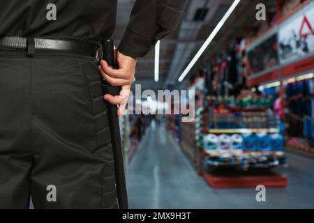 Garde de sécurité en uniforme avec bâton de police dans le centre commercial, à proximité. Espace pour le texte Banque D'Images