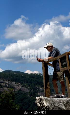 Un homme âgé utilise son téléphone pour prendre une photo de Hickory Nut Falls. Il s'appuie sur le rail de la plate-forme de visualisation. Banque D'Images