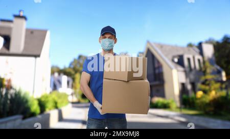 Coursier dans un masque de protection et des gants avec des boîtes dans la rue. Service de livraison pendant la quarantaine du coronavirus Banque D'Images