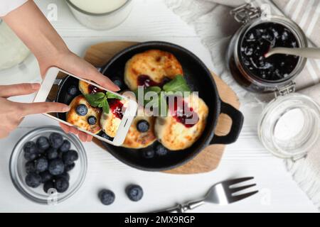 Blogueur de nourriture prenant la photo de délicieux fromage cottage crêpes à la table en bois blanc, gros plan Banque D'Images