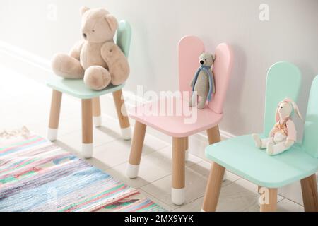 De jolis jouets sur des chaises avec des oreilles de lapin près du mur blanc à l'intérieur. Intérieur de la chambre des enfants Banque D'Images