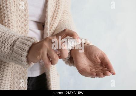 Femme pulvérisant un antiseptique sur la main contre un fond clair, gros plan. Prévention des virus Banque D'Images